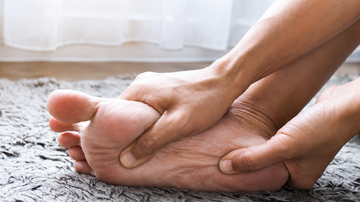 A person sitting at home holding their bare foot, easing the burning and tingling of peripheral neuropathy